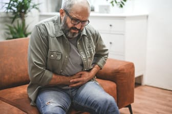 Ein Mann sitzt mit Bauchweh auf dem Sofa