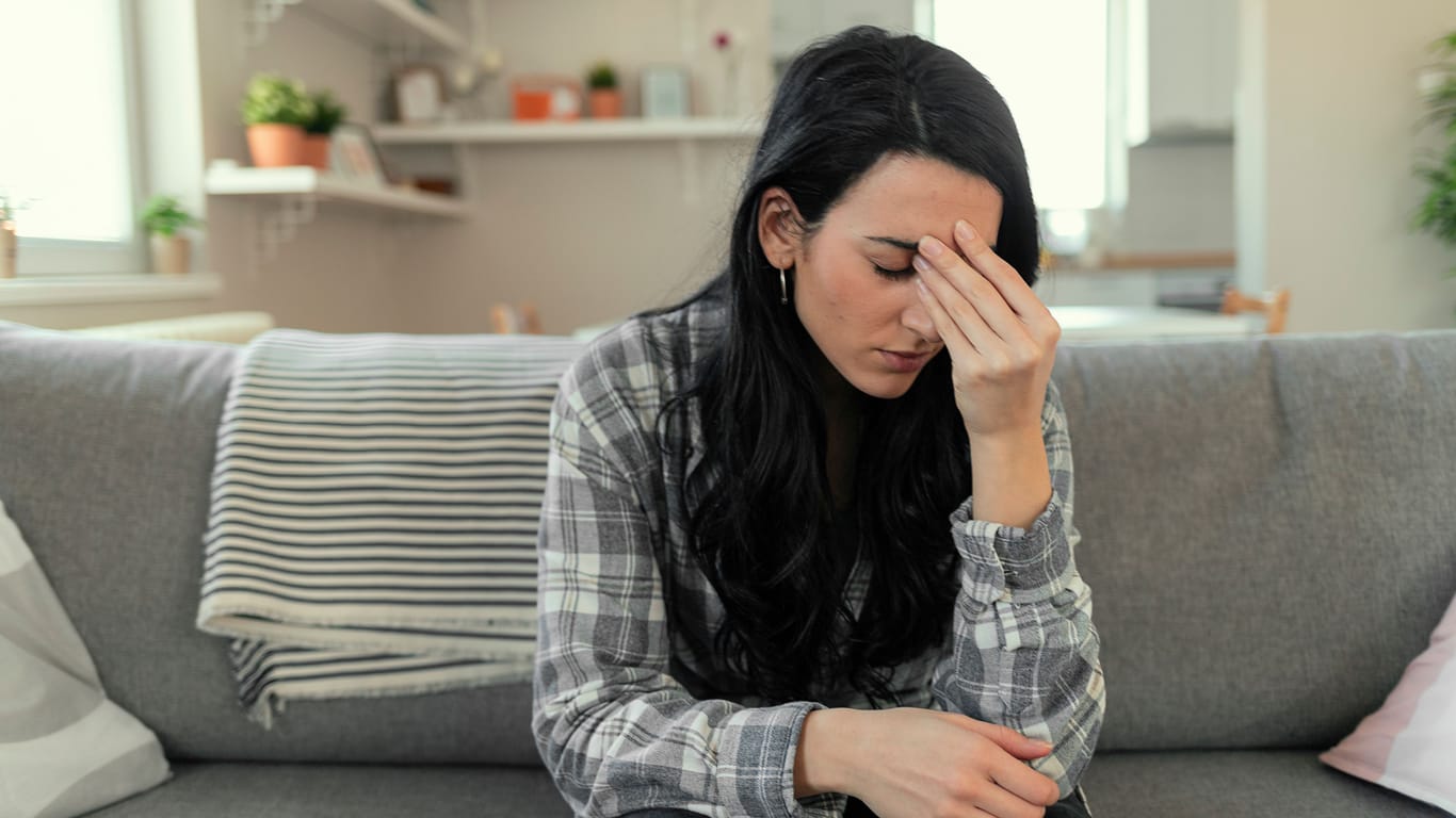 Junge Frau sitzt auf dem Sofa und fühlt sich nicht wohl