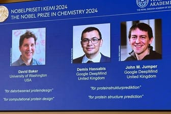 Drei Forscher teilen sich den Preis: Auf der Leinwand während der Pressekonferenz zur Bekanntgabe des Chemie-Nobelpreises 2024 werden Bilder von David Baker, Demis Hassabis, und John M. Jumper gezeigt.