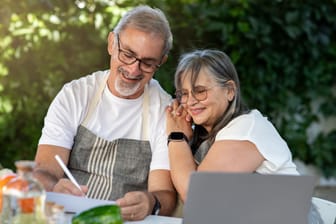 Verheiratetes Paar sitzt im Garten und macht sich Notizen an einem Tisch