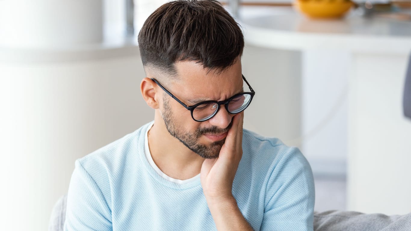 Mann mit Zahnschmerzen: Beschwerden nach einer Zahnextraktion können mit einer Wundheilungsstörung zusammenhängen.