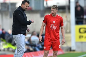 Rot-Weiss-Essen-Trainer Christoph Dabrowski (l) spricht mit seinem Spieler Julian Eitschberger während eines Spiels. Im Hintergrund sind Fans und Werbetafeln zu erkennen. Eitschberger trägt ein rotes Trikot, eine rote Hose und rote Socken.