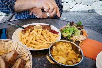 Detail of senior male hand eating from big dish German schnitzel with baked fries and French fries