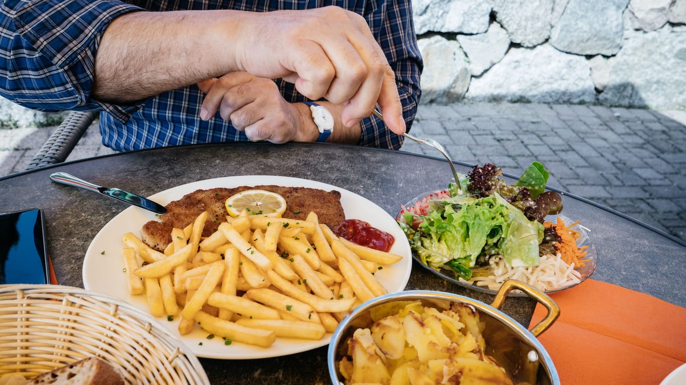 Detail of senior male hand eating from big dish German schnitzel with baked fries and French fries