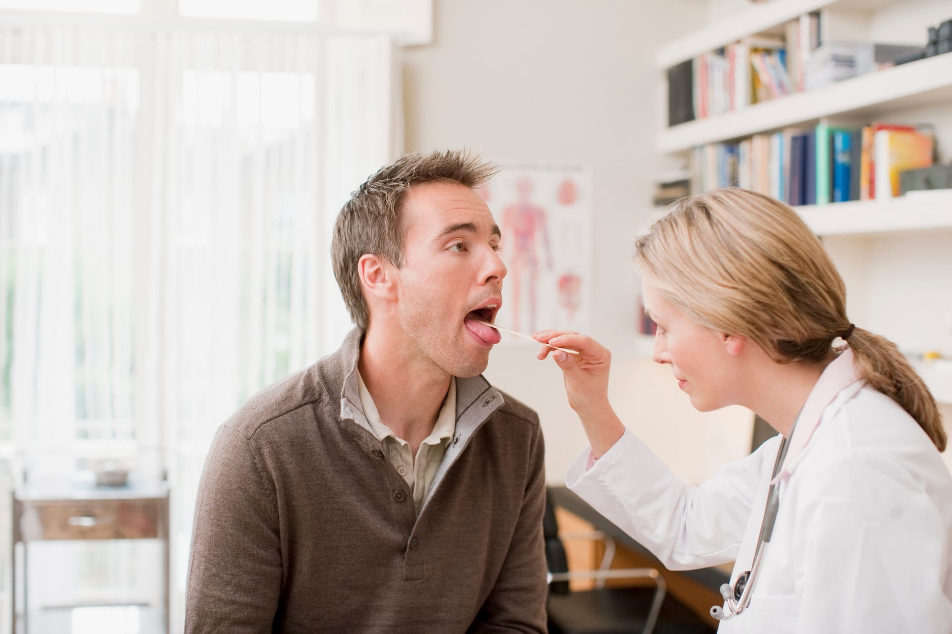 Ärztin untersucht den Rachenraum eines Patienten mit einem Spatel.