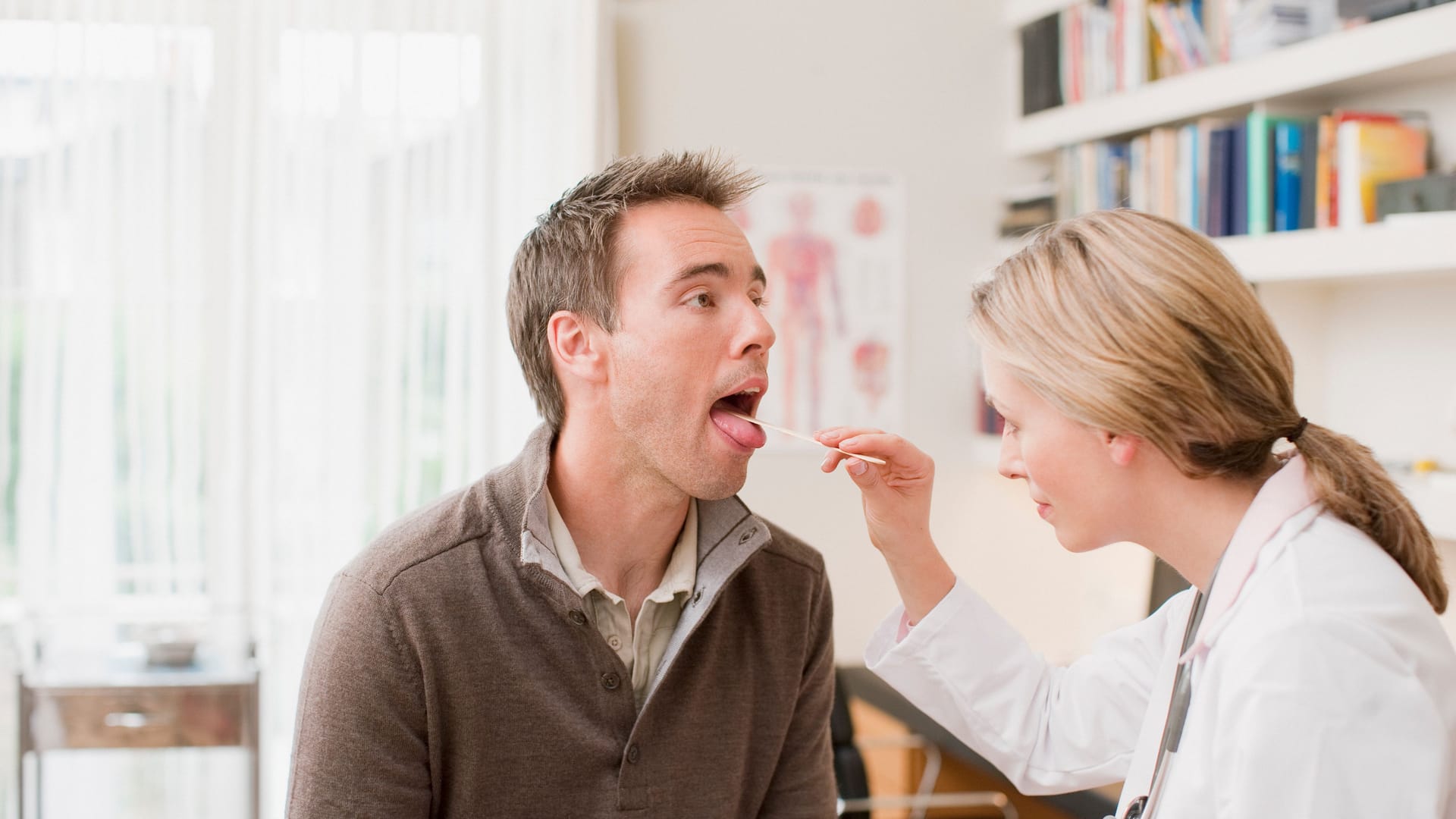 Ärztin untersucht den Rachenraum eines Patienten mit einem Spatel.