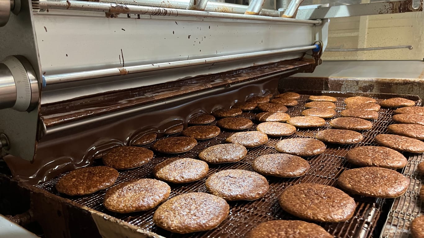 Hier bekommen die Lebkuchen eine Schoko-Dusche verpasst: Danach werden die Leckereien gekühlt und nach der Qualitätskontrolle schließlich verpackt.