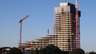 Der in ein Gerüst gehüllte Rohbau des Elbtowers in der Hamburger Hafencity. Drumherum stehen Kräne. Der Himmel ist blau, es ist sonnig.