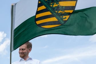 Michael Kretschmer (CDU), Ministerpräsident von Sachsen, schwenkt am Start der Oldtimer Rallye „Sachsen Classic“ eine Sachsen-Fahne.