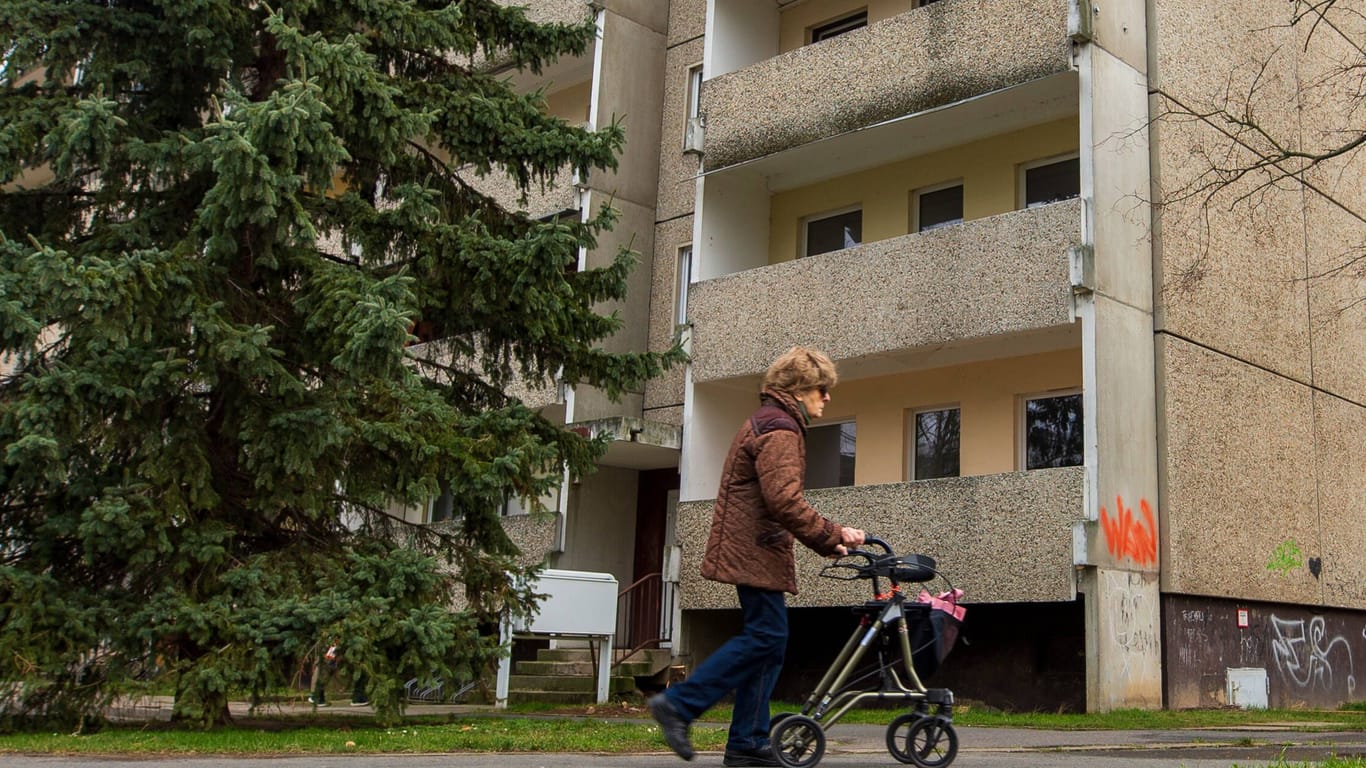 Eine ältere Frau läuft mit ihrem Rollator in der Hand an einem alten Plattenbau im sächsischen Heidenau vorbei. Die ehemalige Industriestadt, hat noch zahlreiche solche DDR-Bauten im Stadtgebiet imago images 151738546