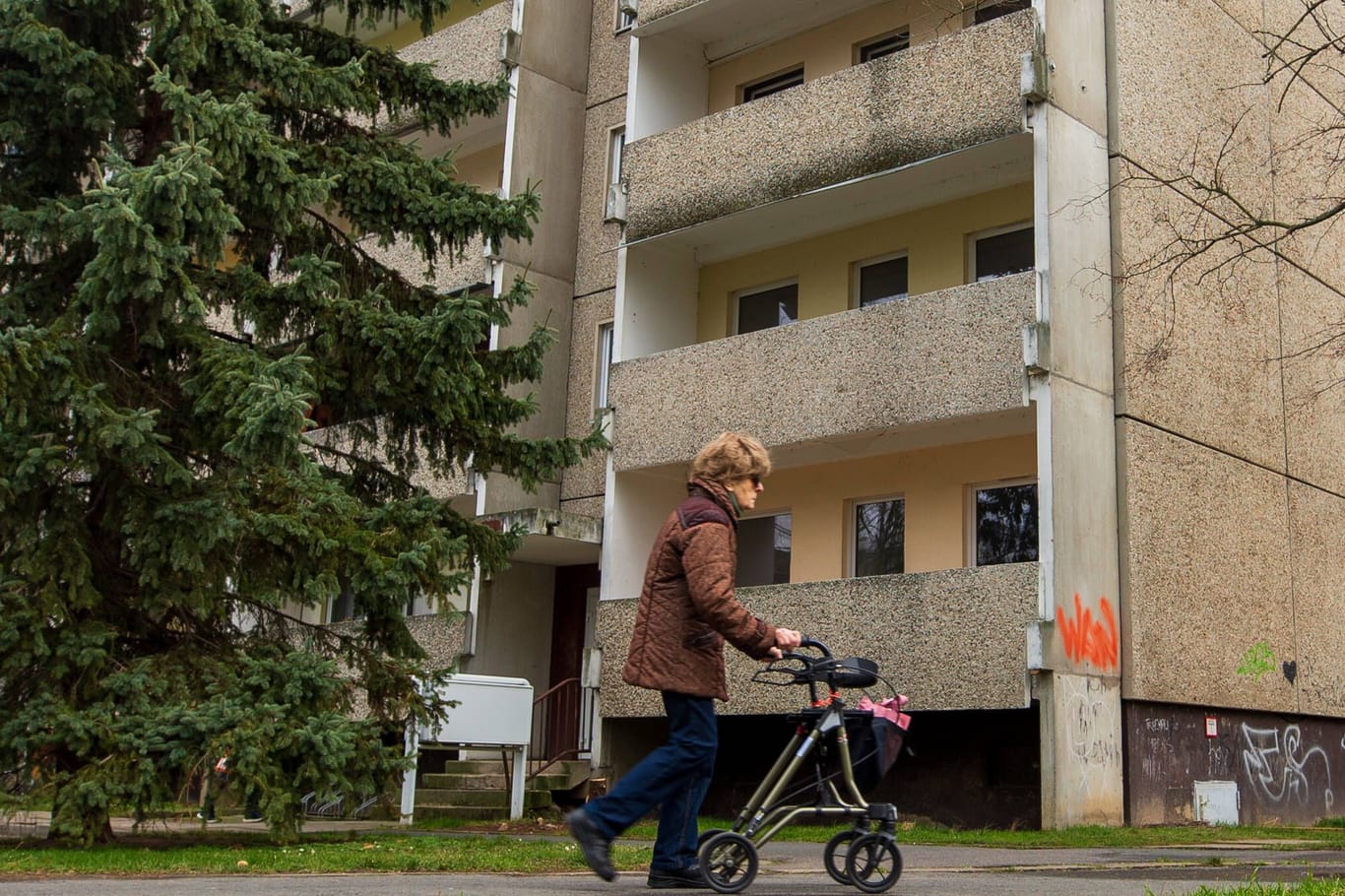 Eine ältere Frau läuft mit ihrem Rollator in der Hand an einem alten Plattenbau im sächsischen Heidenau vorbei. Die ehemalige Industriestadt, hat noch zahlreiche solche DDR-Bauten im Stadtgebiet imago images 151738546