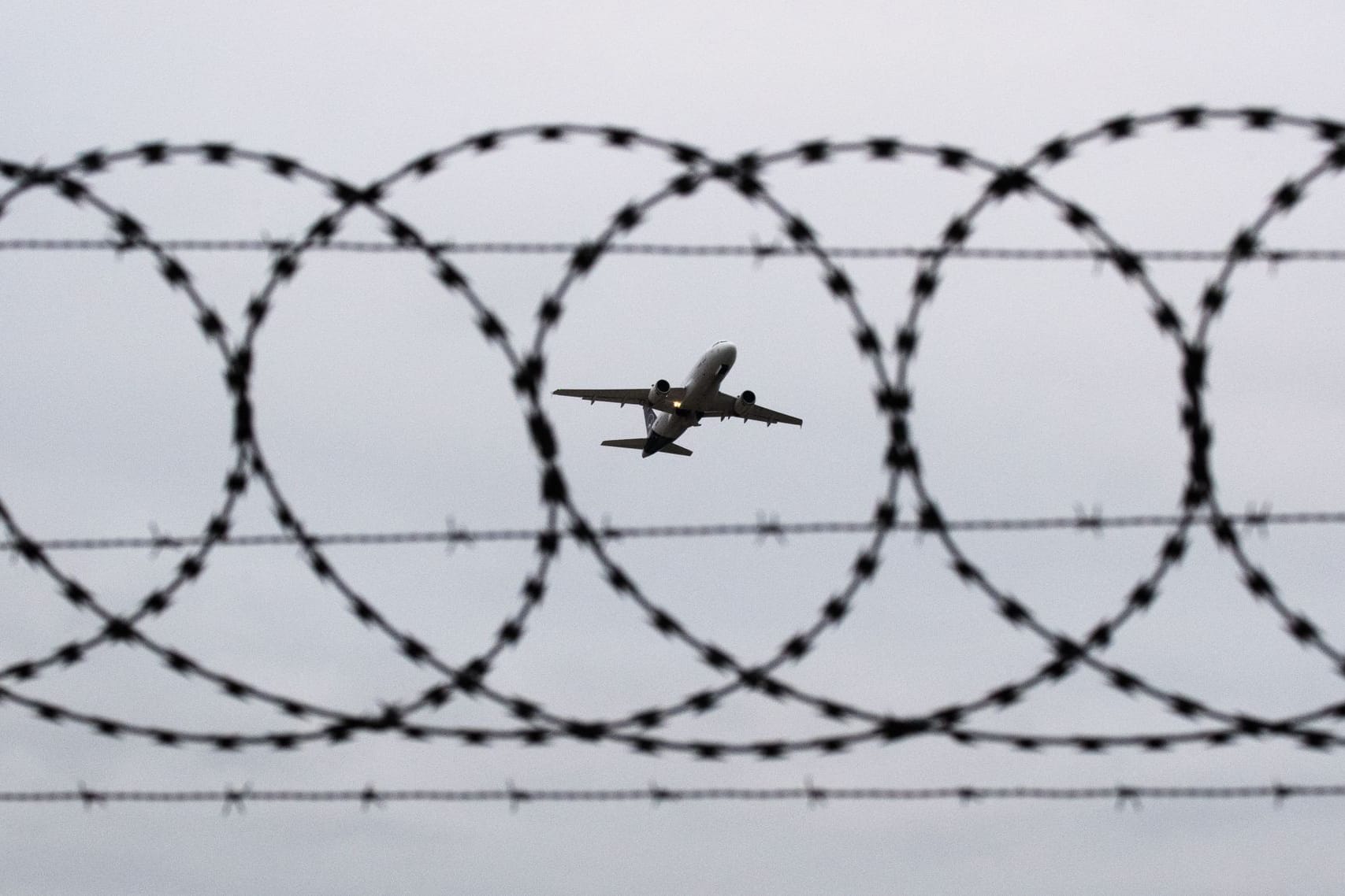 Flugzeug fotografiert durch Stacheldraht am Flughafenzaun (Symbolbild): In Hamburg igbt es eine Debatte um Abschiebung aus dem Kirchenasyl.