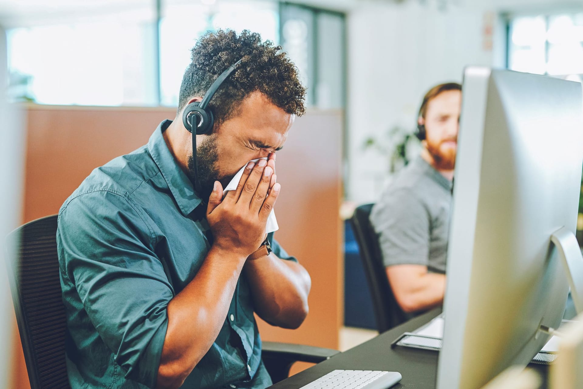 Mann sitzt mit Erkältung vor dem Computer im Büro