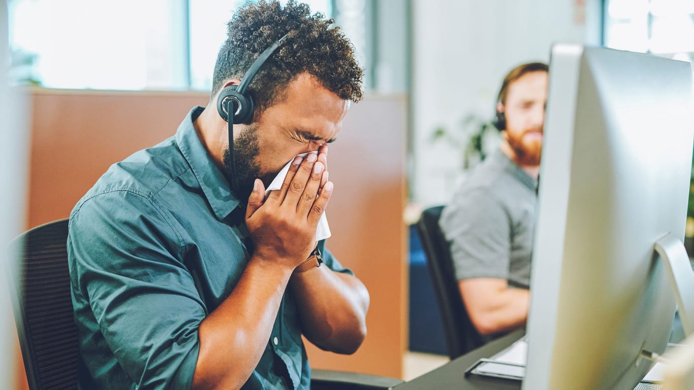 Mann sitzt mit Erkältung vor dem Computer im Büro