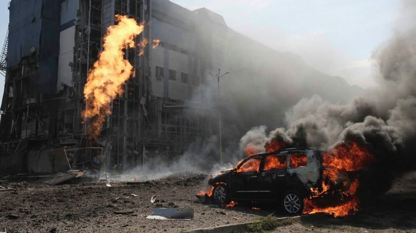 Nach zwei russischen Bombenanschlägen brennt ein Auto vor einem Geschäftszentrum, das durch die Angriffe beschädigt wurde.