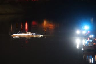 Teile eines Schiffes schwimmen im Wasser im Mannheimer Industriehafen, während Boote im Einsatz sind.