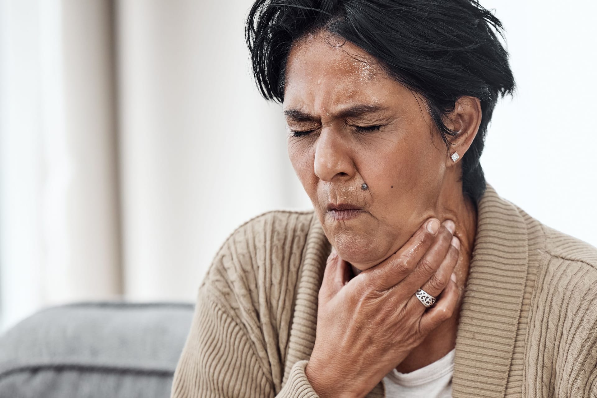 Senior woman, cough and sick on sofa in home, chest pain and pneumonia with tuberculosis or choke. Pensioner, mature lady or sore throat with lung infection, breathing problem and choking with asthma