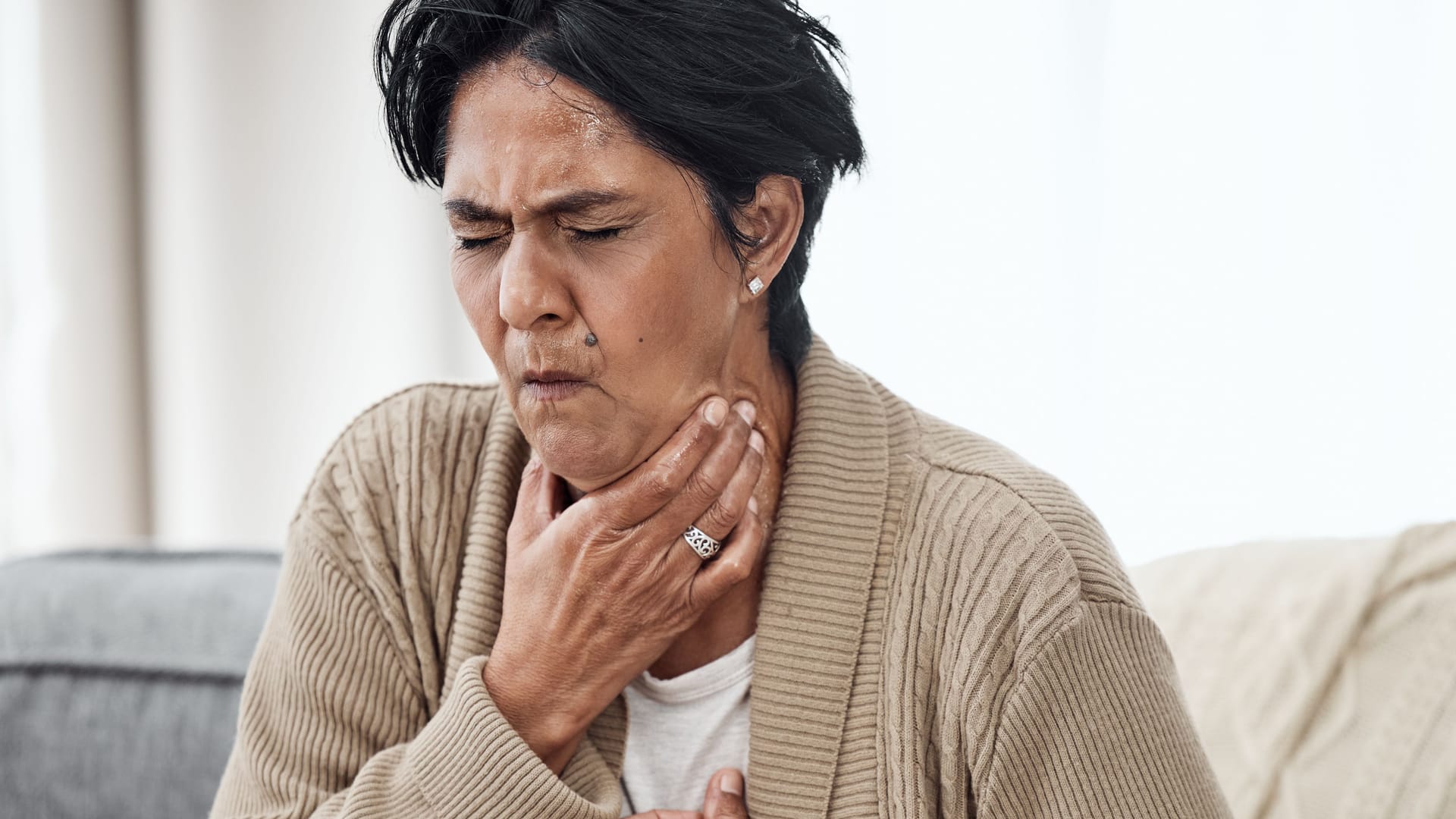 Senior woman, cough and sick on sofa in home, chest pain and pneumonia with tuberculosis or choke. Pensioner, mature lady or sore throat with lung infection, breathing problem and choking with asthma