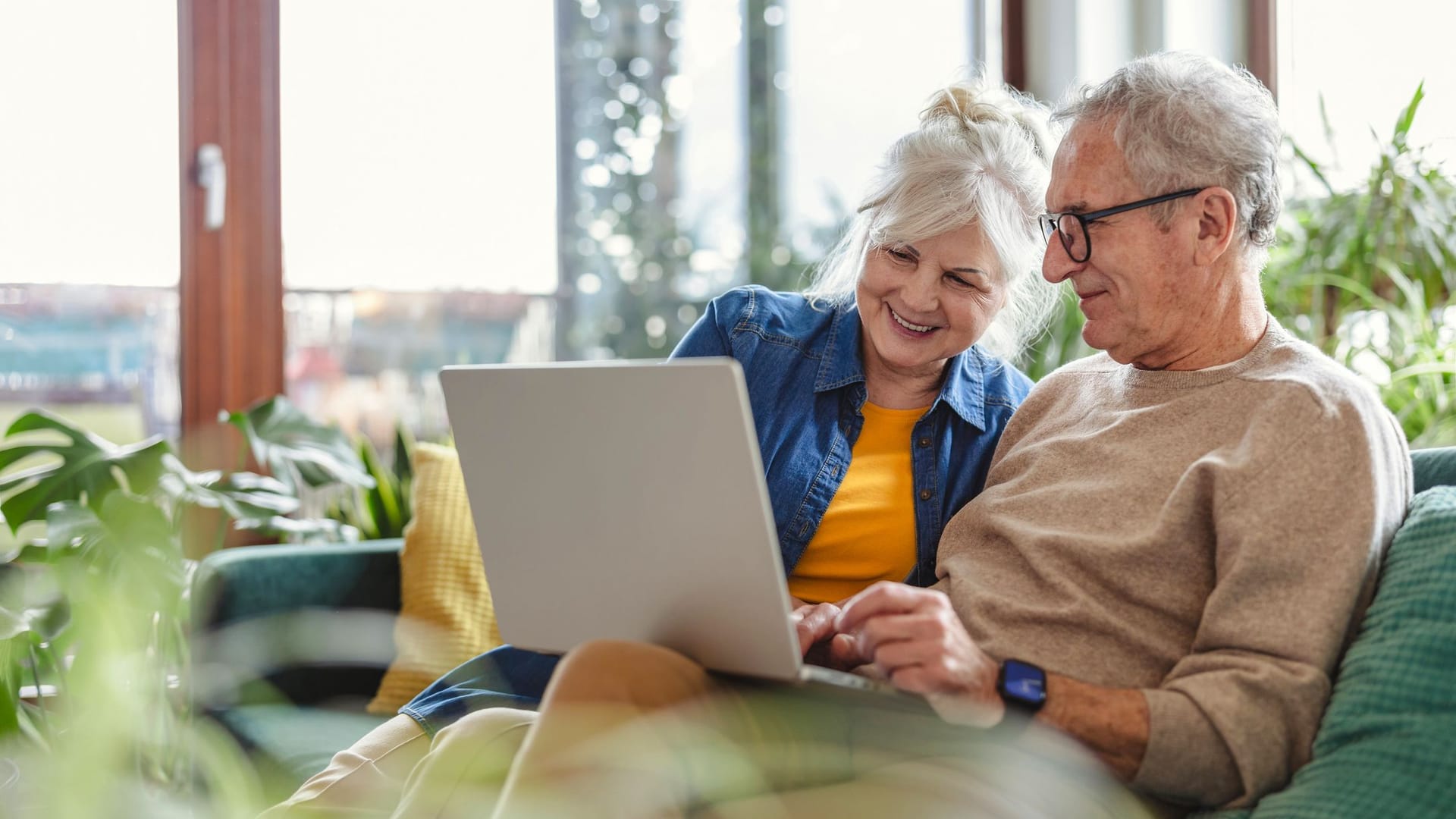 Rentnerpaar sitzt auf dem Sofa und schaut auf den Laptop