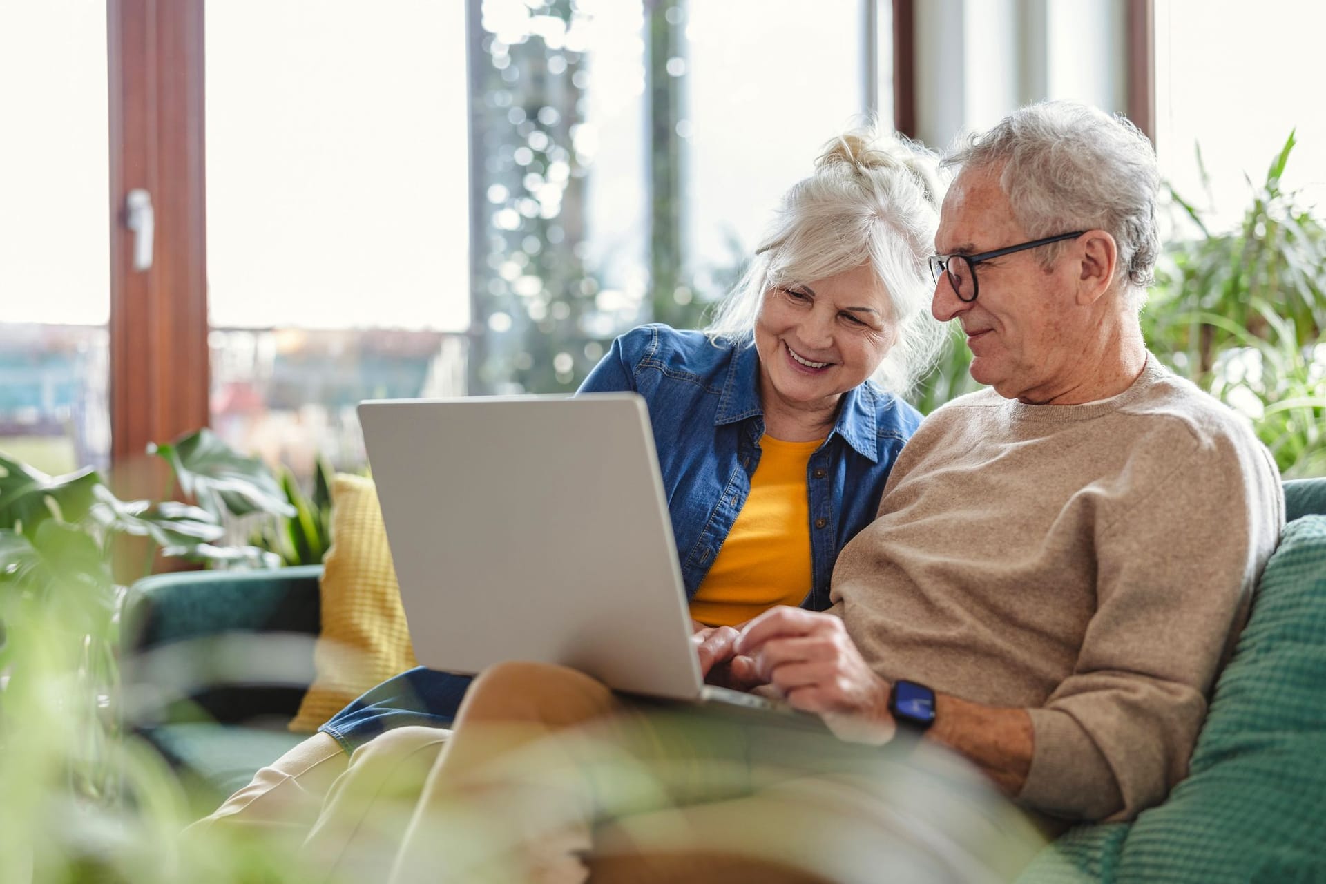 Rentnerpaar sitzt auf dem Sofa und schaut auf den Laptop