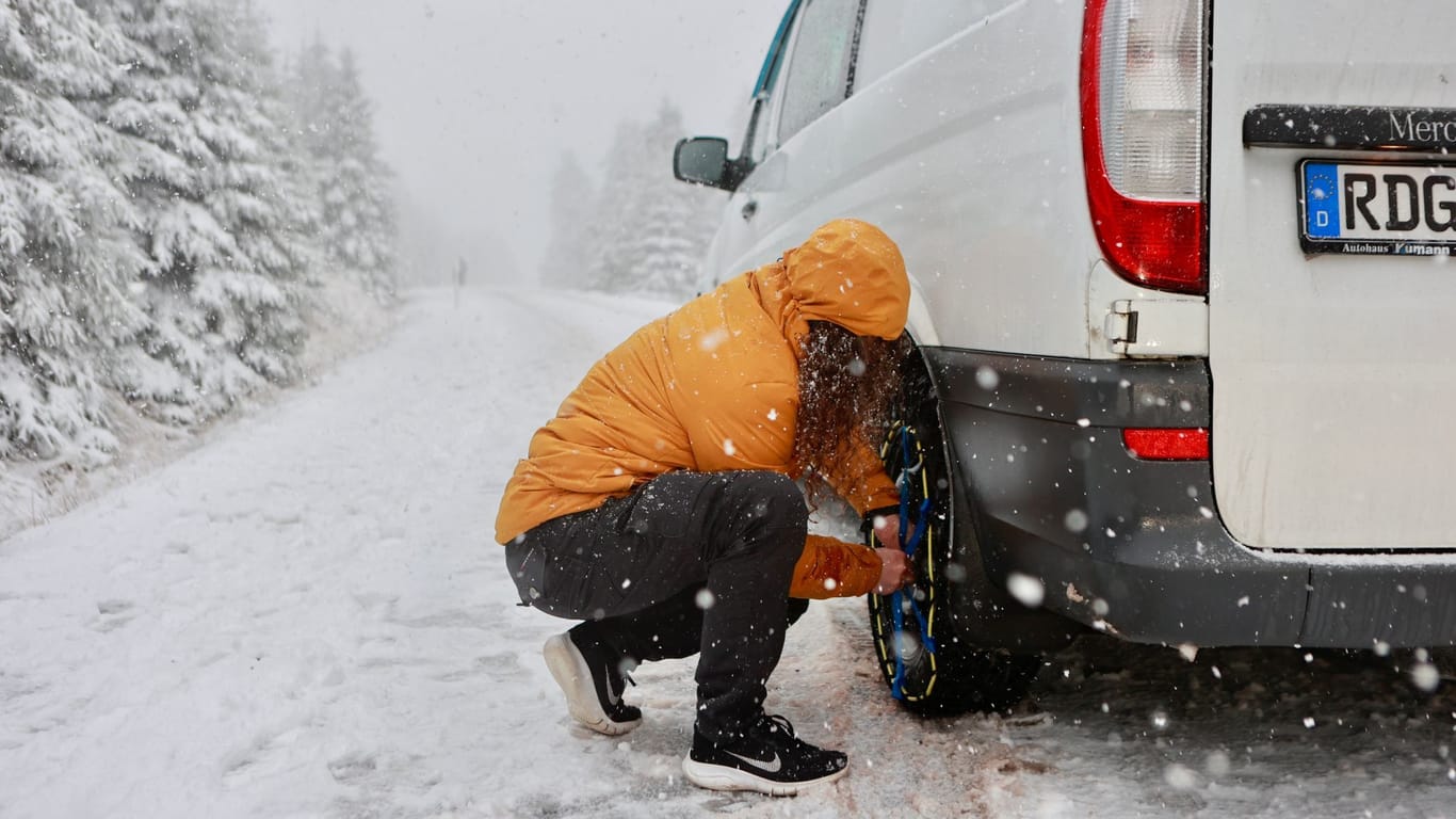 Schneeketten werden auf der eisglatten Brockenstraße auf die Reifen eines Transporters aufgezogen.