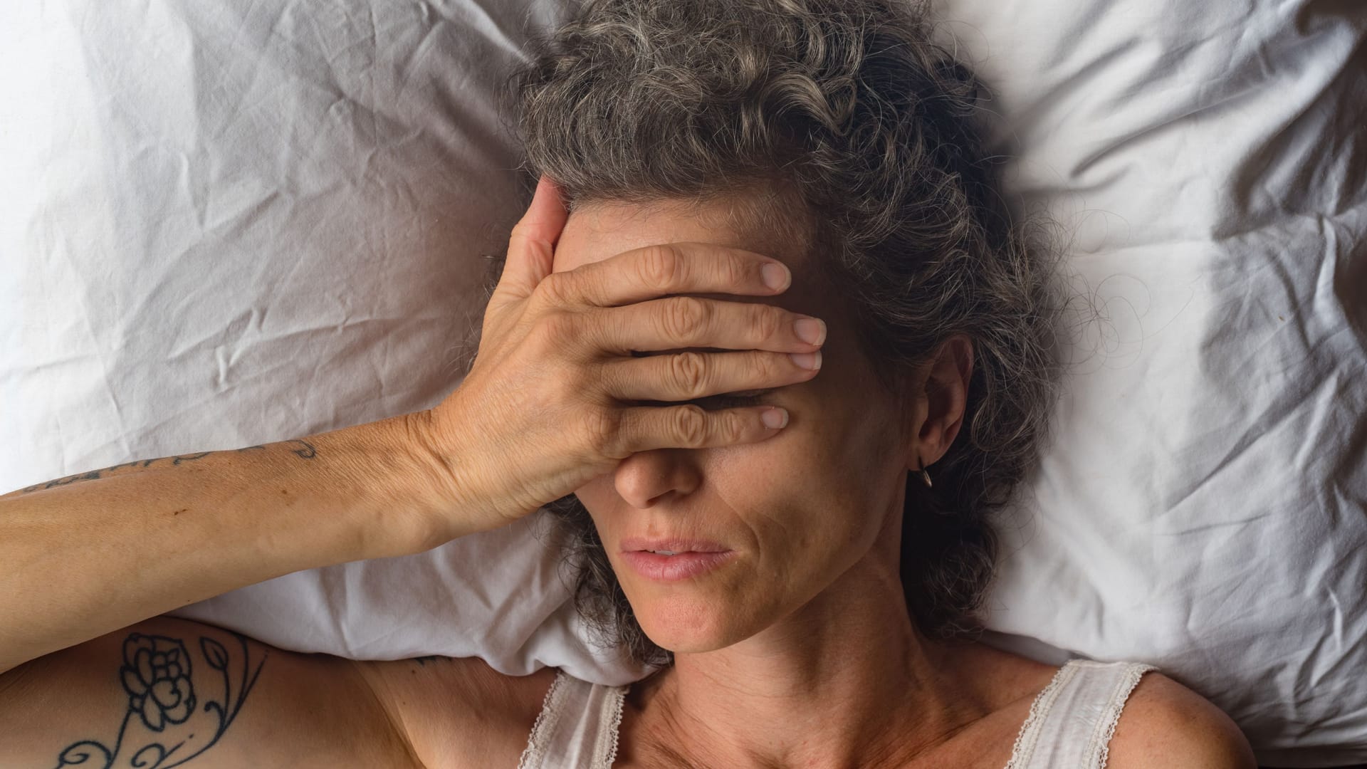 Eine im Bett liegende Frau legt eine Hand über Augen und Stirn