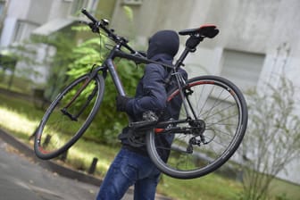 Ein maskierter Mann trägt ein geklautes Fahrrad (Symbolbild): Die Bundespolizei ermittelt wegen eines besonders schweren Falls des Diebstahls.