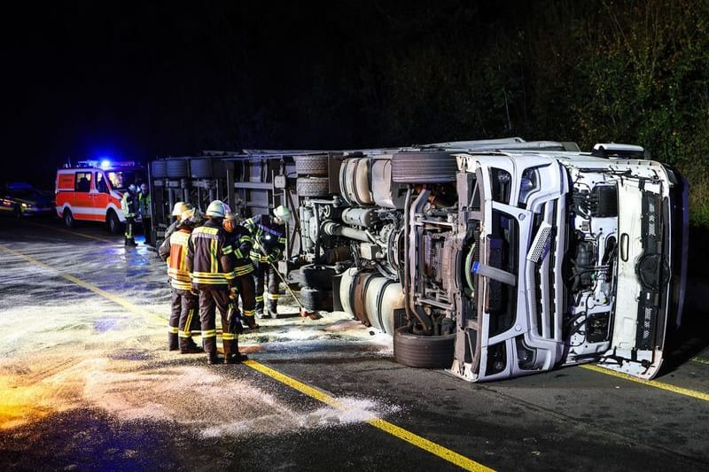 Einsatzkräfte der Feuerwehr stehen auf der Autobahn A45 neben einem umgekippten Bierlaster.