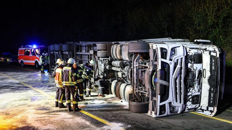 Einsatzkräfte der Feuerwehr stehen auf der Autobahn A45 neben einem umgekippten Bierlaster.