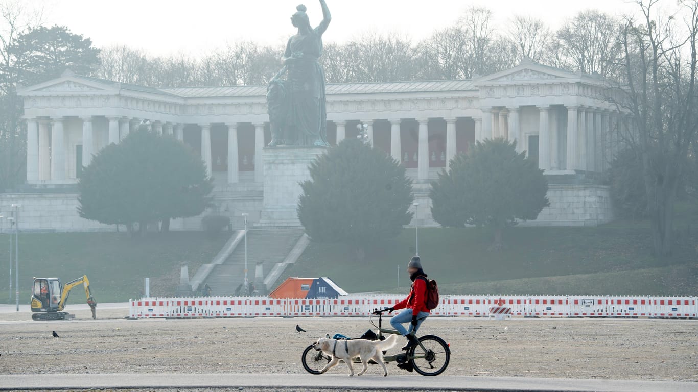 Ein Mann fährt mit seinem Fahrrad vor der Bavaria auf der Theresienwiese (Archivbild): Die Sonne hat es am Dienstag schwer, sich gegen den Nebel durchzusetzen.