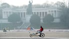 Ein Mann fährt mit seinem Fahrrad vor der Bavaria auf der Theresienwiese (Archivbild): Die Sonne hat es am Dienstag schwer, sich gegen den Nebel durchzusetzen.