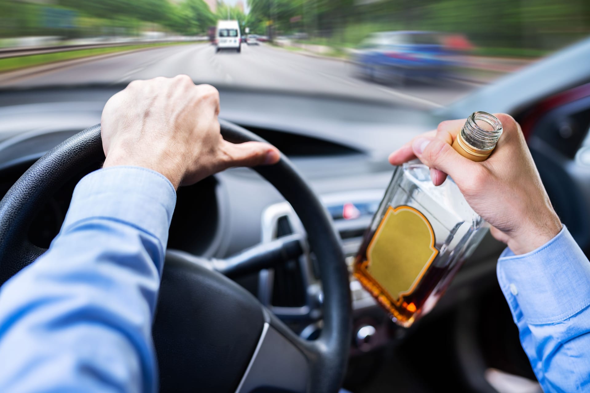 Ein Autofahrer hält eine Schnapsflasche in der Hand (Symbolbild):