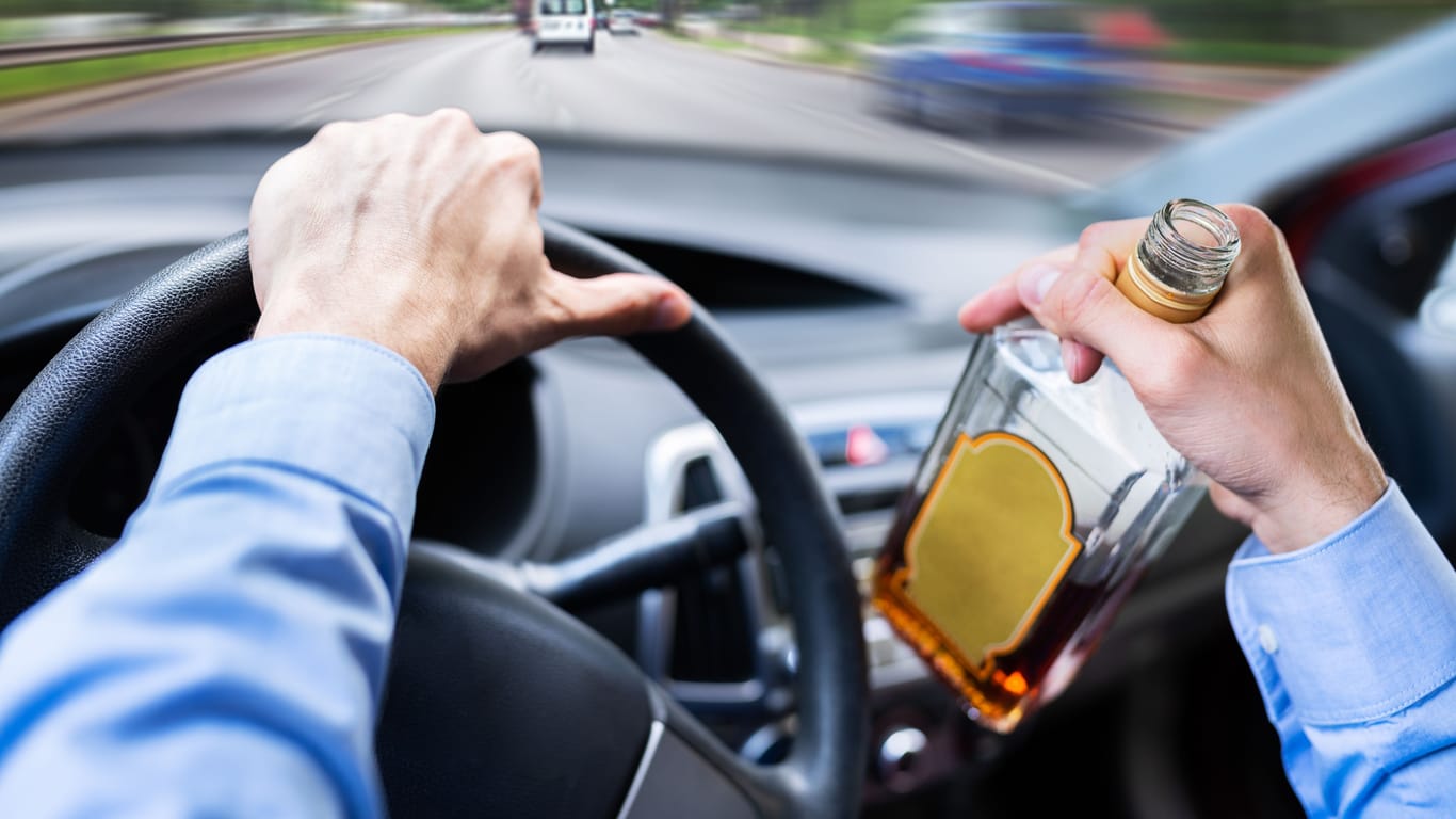 Ein Autofahrer hält eine Schnapsflasche in der Hand (Symbolbild):