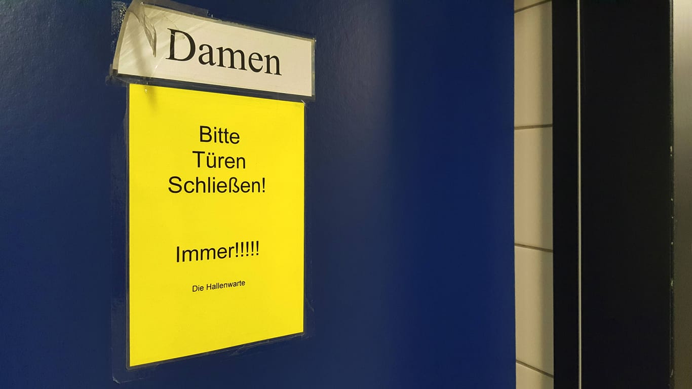 Hinweisschild "Bitte Türen schließen!" an der Tür einer Damenunkleide: Der Mann hatte sein Handy unter Trennwänden von Umkleidekabinen hindurchgeschoben.