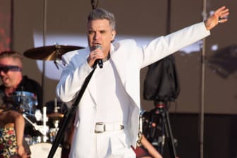 Robbie Williams singt auf der Bühne (Archivbild): Der Weltstar spielt 2025 ein Stadionkonzert in Hannover.