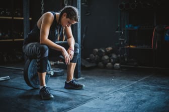 Eine Sportlerin liegt erschöpft auf dem Boden, neben ihr sind Hanteln zu sehen.