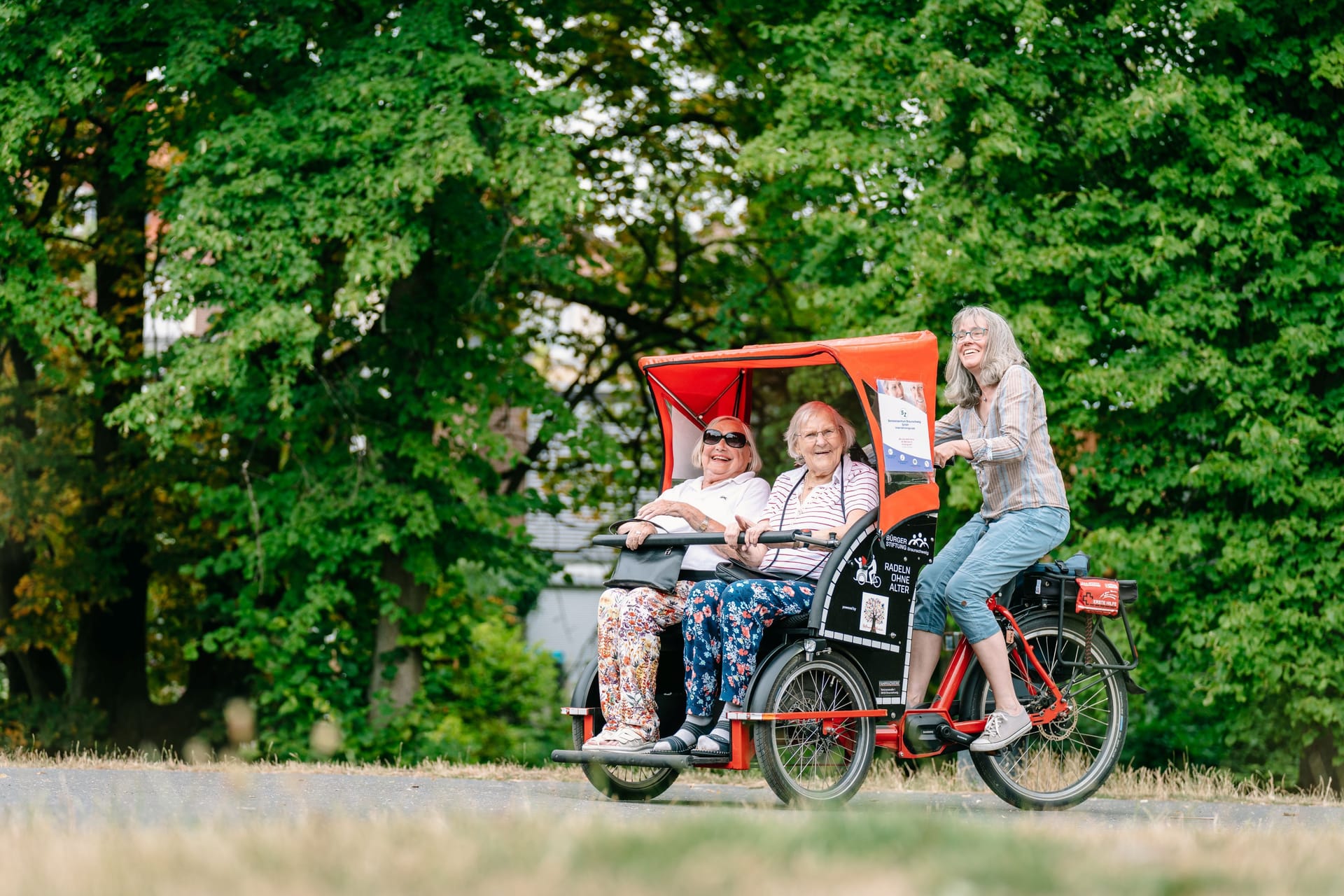 Eine Ehrenamtliche der Bürgerstiftung radelt zwei ältere Damen durch den Inselwallpark. Drei der roten Rikschas stehen an zwei Tagen für Friedhofbesucher zur Verfügung.