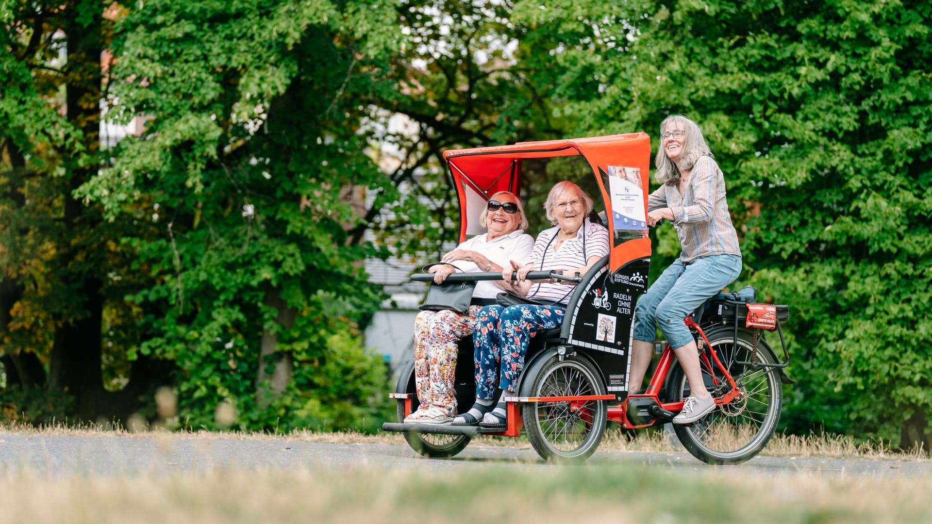 Eine Ehrenamtliche der Bürgerstiftung radelt zwei ältere Damen durch den Inselwallpark. Drei der roten Rikschas stehen an zwei Tagen für Friedhofbesucher zur Verfügung.