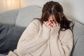 Eine Frau sitzt verängstigt auf einem Sofa (Symbolbild): Nach Fußballspielen ist die Gefahr, Opfer häuslicher Gewalt zu werden, besonders hoch.