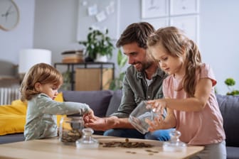 Vater mit seinen Kindern zählt Geld aus der Spardose