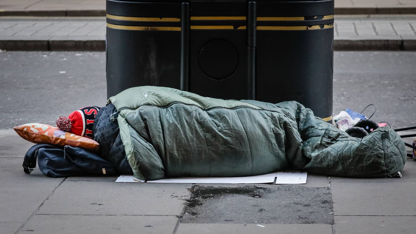 Eine obdachlose Person liegt in einem Schlafsack auf der Straße (Archivbild):