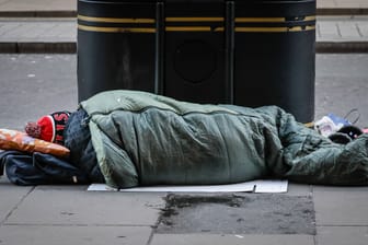 Eine obdachlose Person liegt in einem Schlafsack auf der Straße (Archivbild):