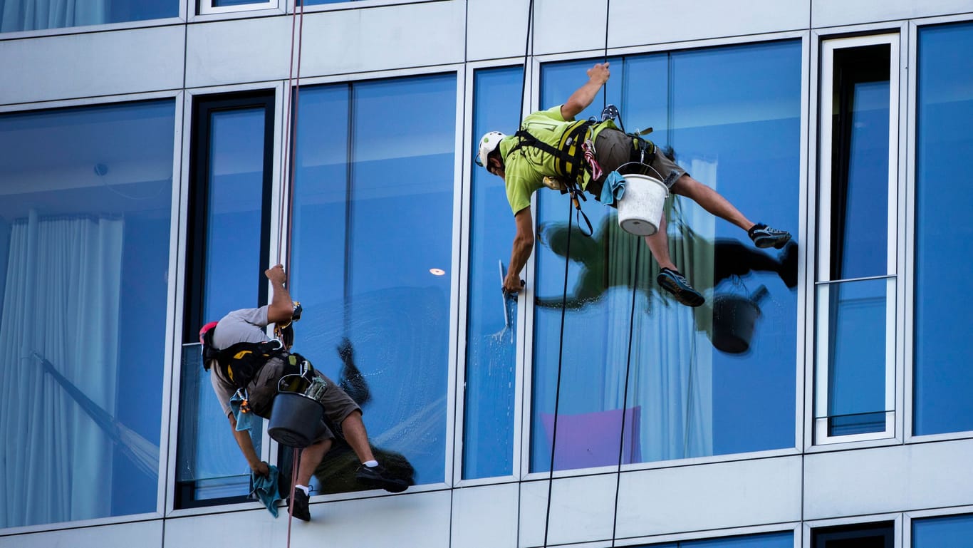 Fensterputzer reinigen eine Glasfassade: Gebäudereiniger erhalten ab 2025 mehr Geld.