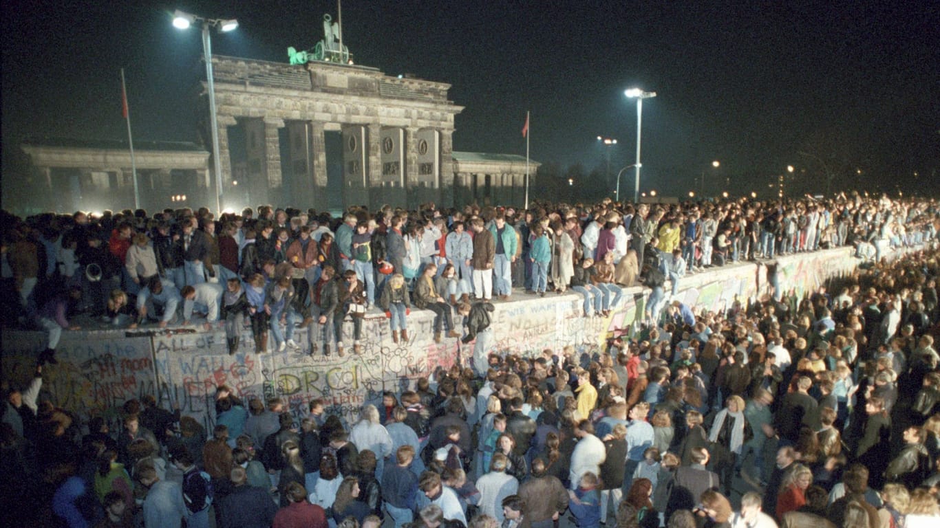 Menschen auf der Berliner Mauer vor dem Brandenburger Tor in der Nacht vom 9. auf den 10.11.1989: In Berlin wird auf vielfältige Weise an den Fall der Mauer vor 35 Jahren erinnert.