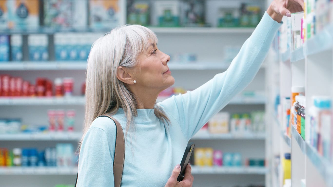 Eine Frau in der Apotheke greift nach einem Produkt aus dem Regal