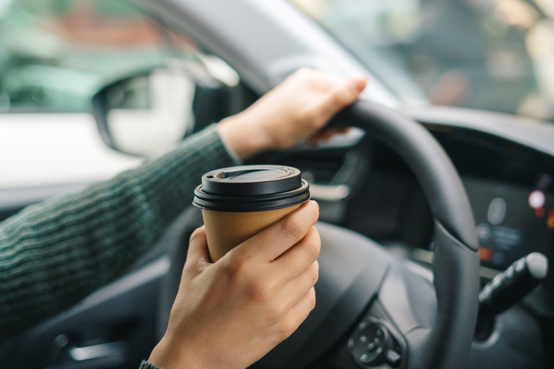 Eine Autofahrerin hält einen Kaffeebecher in der Hand: Kaffee allein kann Sekundenschlaf nicht verhindern.