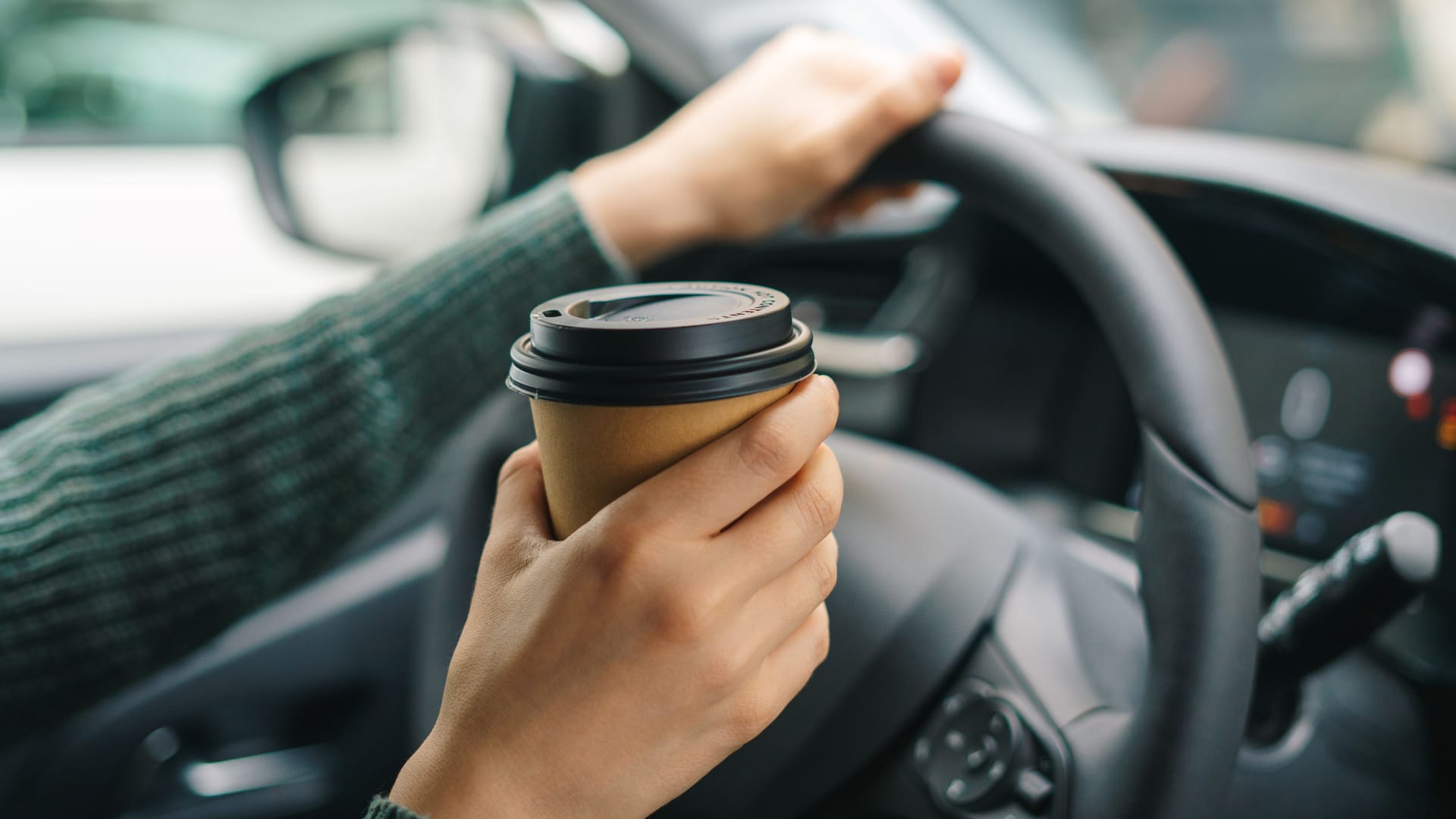 Eine Autofahrerin hält einen Kaffeebecher in der Hand: Kaffee allein kann Sekundenschlaf nicht verhindern.