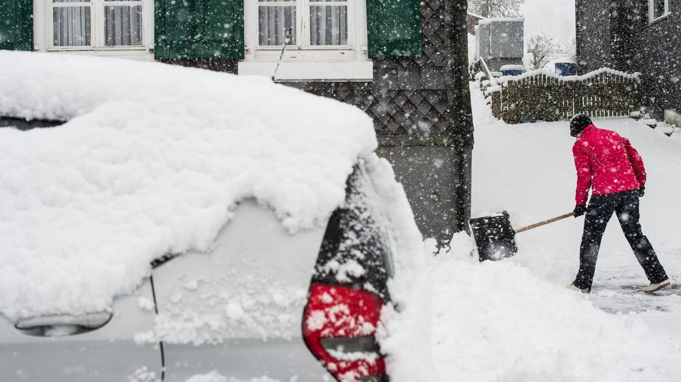 Eine Frau räumt Neuschnee aus der Zufahrt zu einem Haus