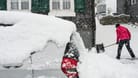 Eine Frau räumt Neuschnee aus der Zufahrt zu einem Haus