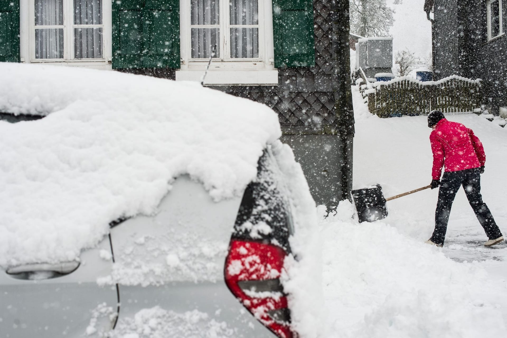 Eine Frau räumt Neuschnee aus der Zufahrt zu einem Haus